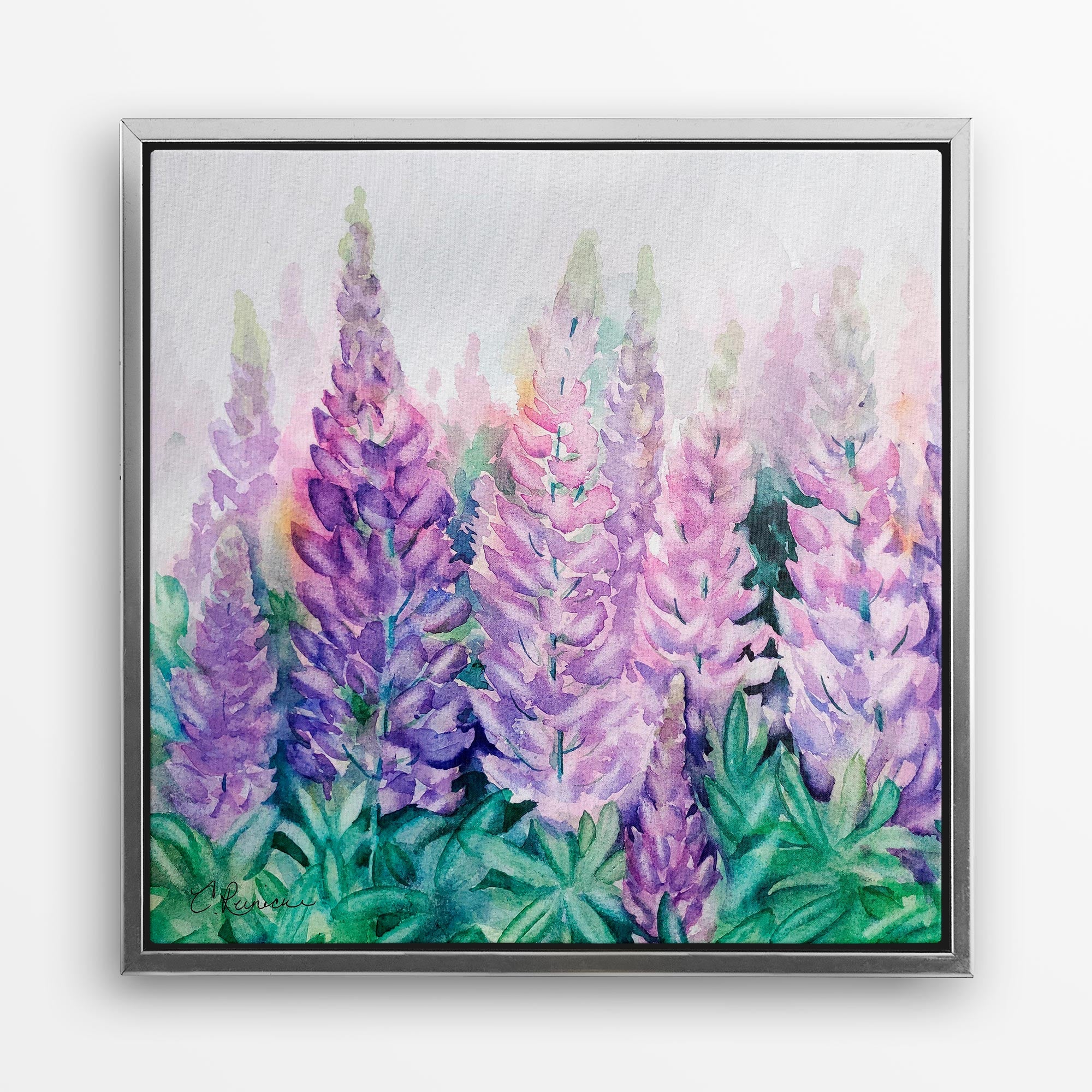 A gold-framed wall art canvas of a lupine wildflower print. The print is of a group of lupine wildflowers in various shades of purple and blue. The flowers are in a field of green leaves. The background is silver. The image is signed by the artist, Conni Reinecke in the bottom left corner.